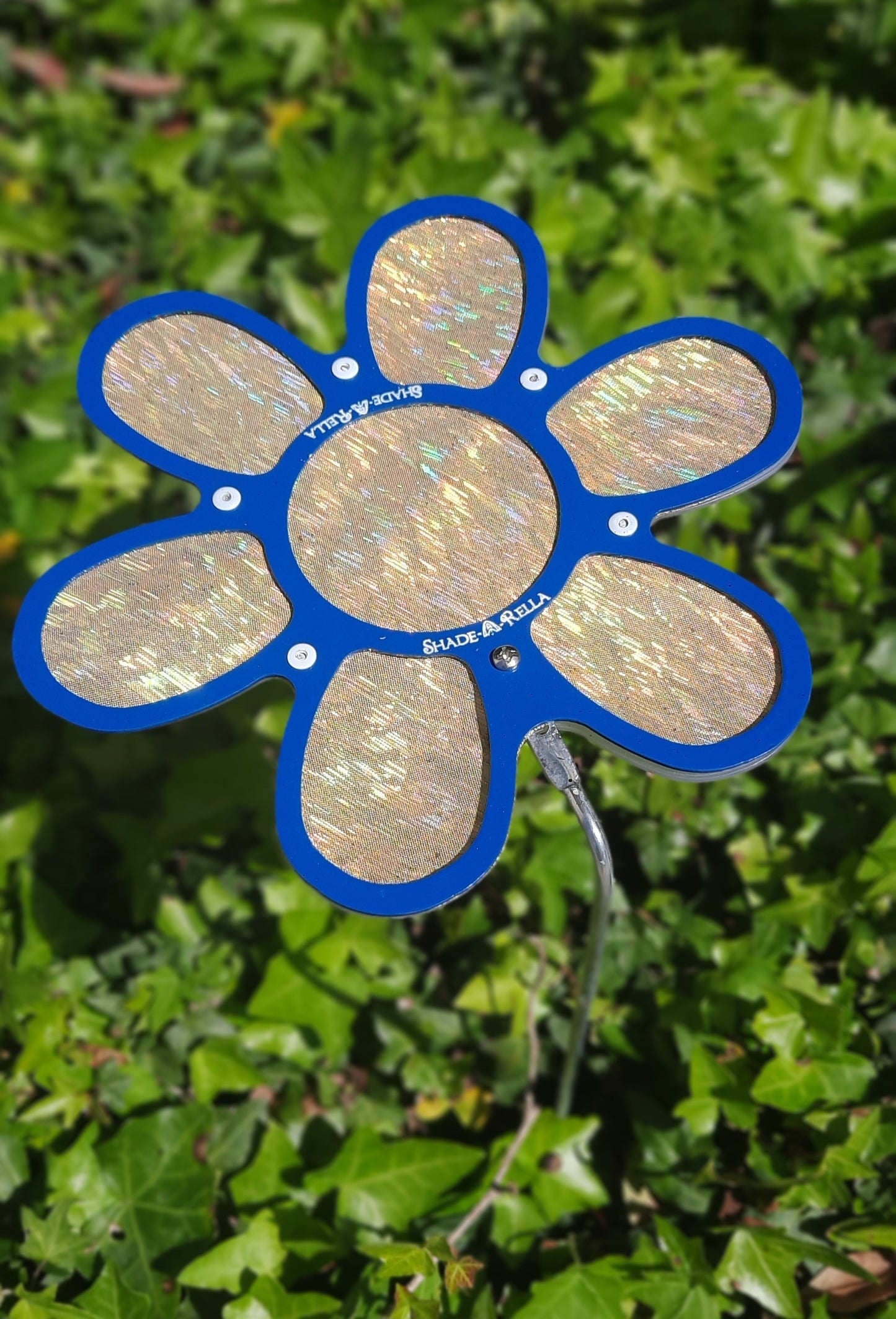 The Shade-A-Rella 7.5 small Shimmer Flowers plant shade, a shiny blue and gold flower-shaped ornament on a metal stem, adds elegant plant umbrella style to your garden while offering shade among lush greenery.