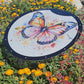 The 24" Butterfly Shade-A-Rella by Shade-A-Rella is a durable plant umbrella featuring a colorful butterfly design and 70% shading cloth, providing garden shade among blooming yellow, orange, and red flowers.