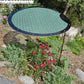 The Shade-A-Rella Circle Shade-A-Rella adjustable plant umbrella features a round green mesh disk with a powder-coated frame and steel shade holder, shading pink and purple flowers amid rocks, mulch, and lush plants.
