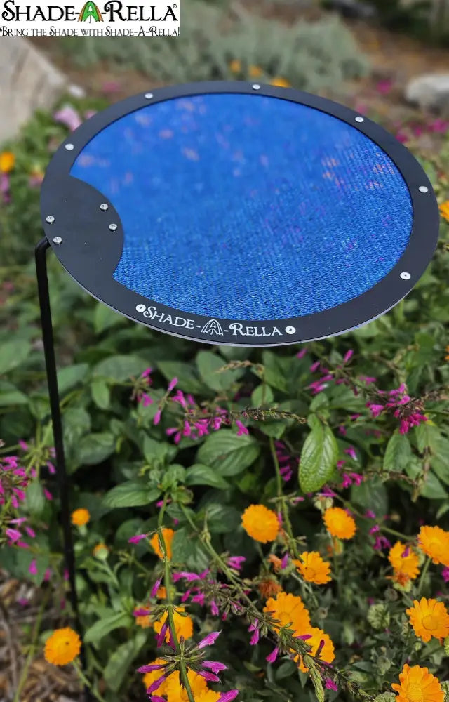 The Shade-A-Rella Circle Shade-A-Rella plant shade is a small, circular blue mesh umbrella with a black rim on an adjustable rod and steel holder, shown among flowering garden plants. Choose your size from this Adjustable Plant Umbrella by Shade-A-Rella.