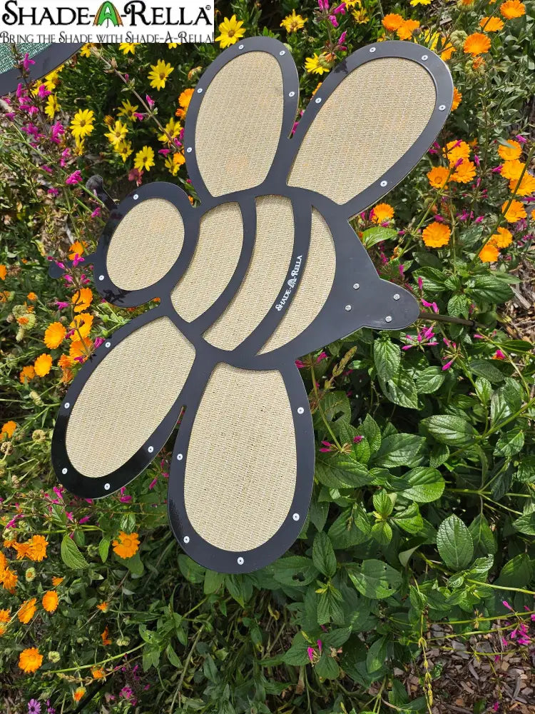 The Shade-A-Rella Super Sale! 24 inch Bee with black frame and light yellow 90% shade cloth adds charm among green plants and vibrant blooms, while the subtle holder supports overhead plant shade.